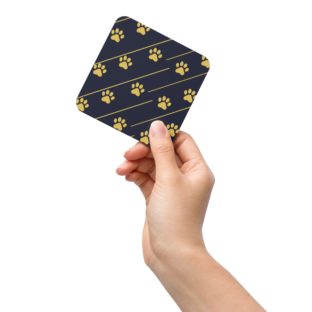 Hand holding a blue coaster with gold paw prints on a white background