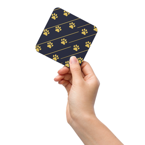 Hand holding a blue coaster with gold paw prints on a white background