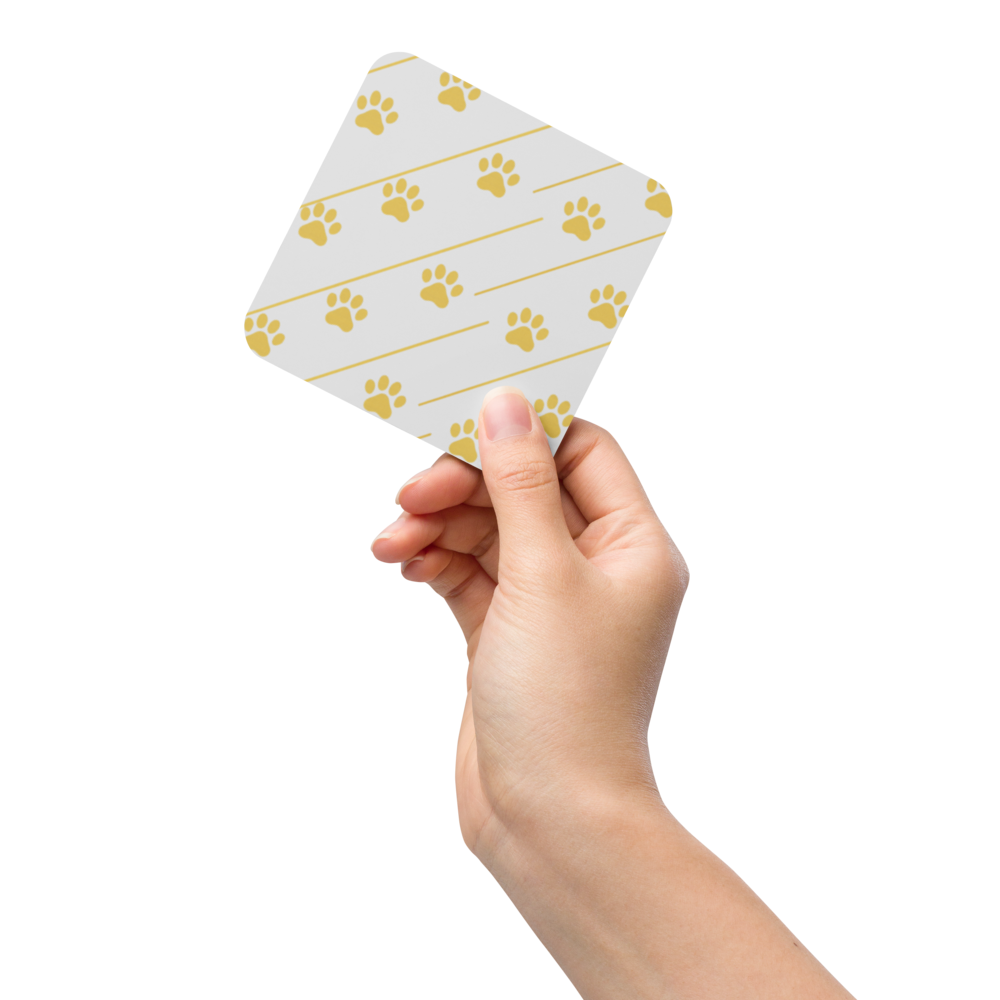 Hand holding a small ivory whisper coaster with gold paw print pattern on a white background