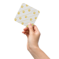 Hand holding a small ivory whisper coaster with gold paw print pattern on a white background