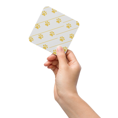Hand holding a small ivory whisper coaster with gold paw print pattern on a white background