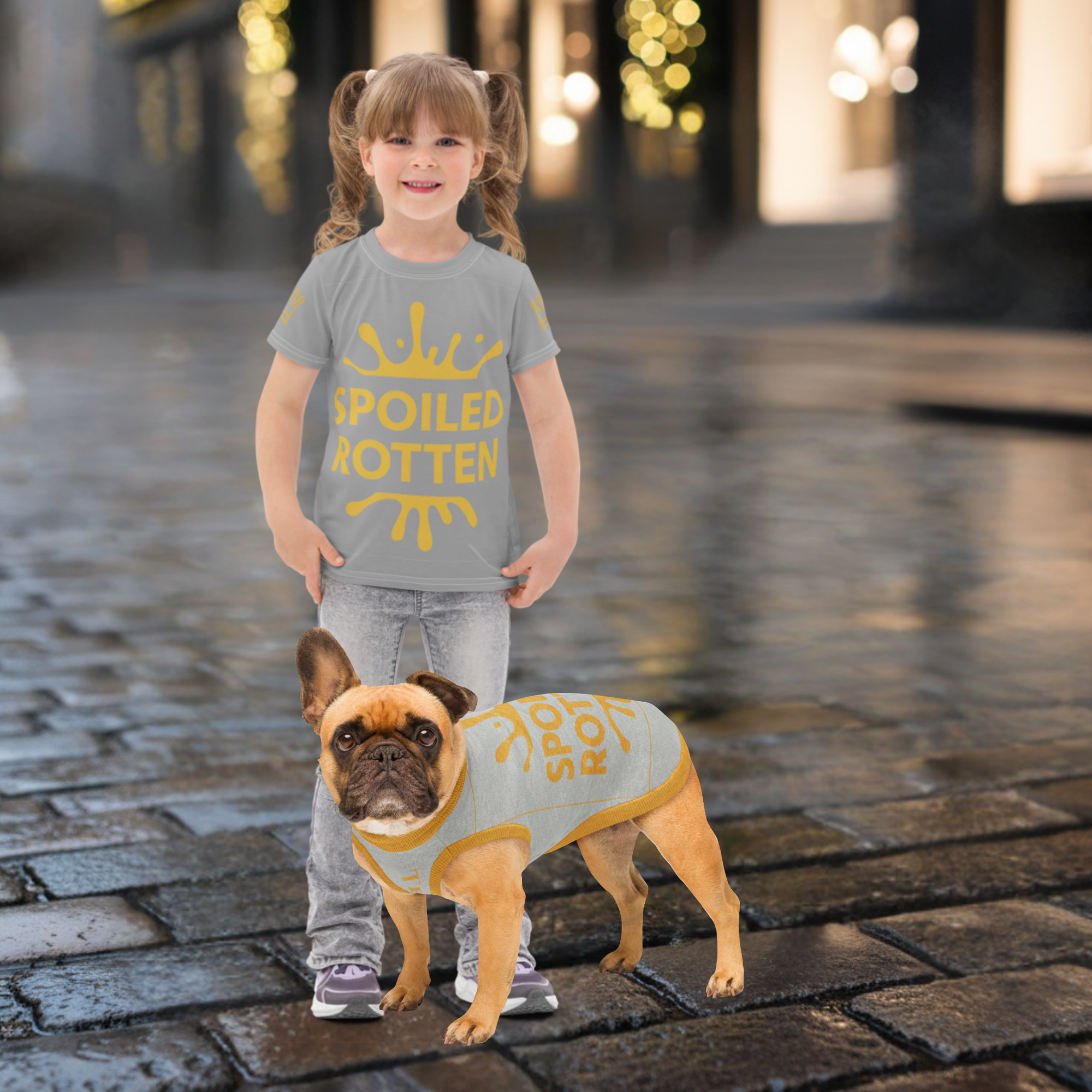 Child wearing a 'Spoiled Rotten' shirt with a dog in a matching outfit on a cobblestone street.