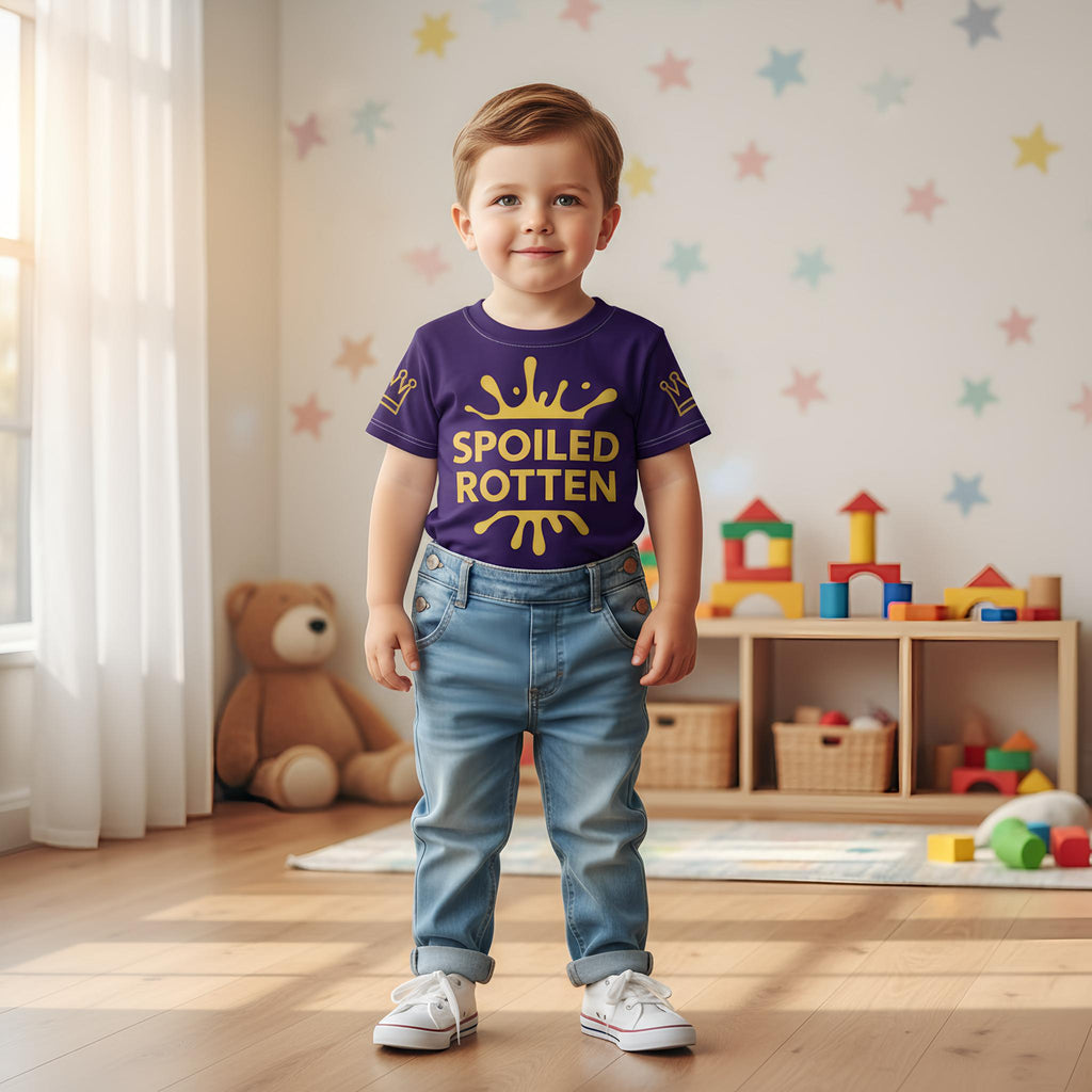 Child wearing a blue t-shirt with yellow text in a room with toys and a teddy bear.