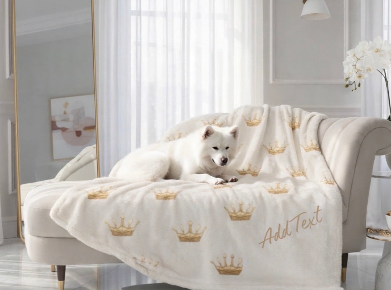 White dog lying on a cream-colored sofa with a decorative blanket featuring gold crowns and text.