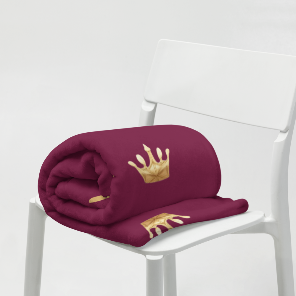 Folded maroon blanket with gold crown design on a white chair