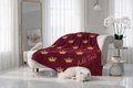 Red blanket with gold crowns and 'Add Text' on a white sofa in a bright room.