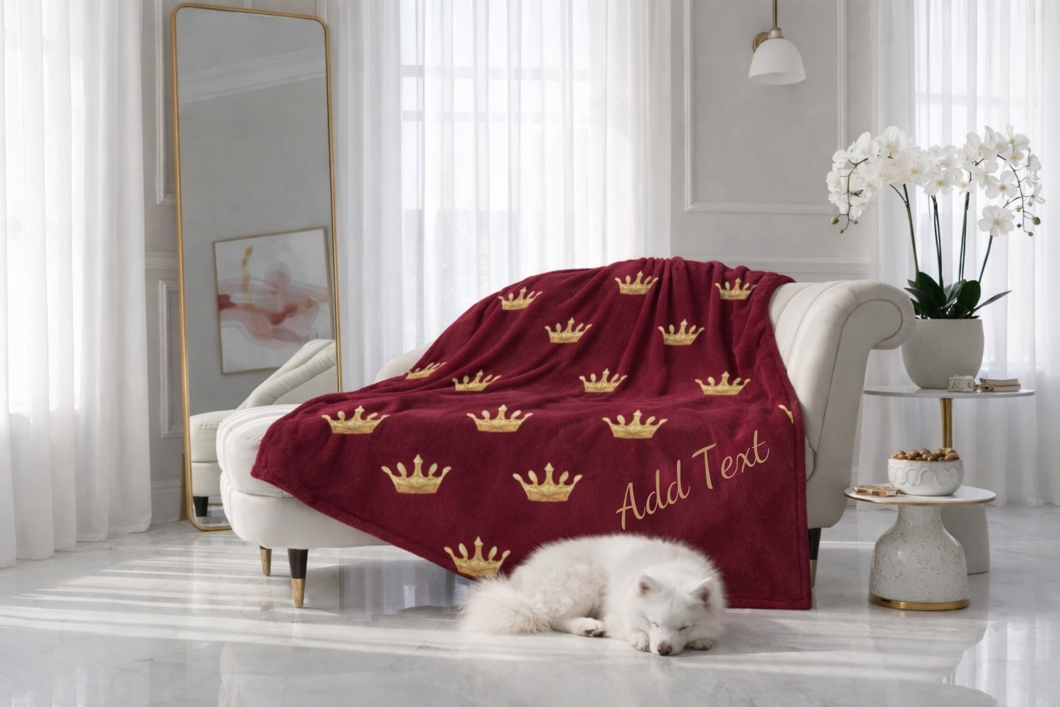 Red blanket with gold crowns and 'Add Text' on a white sofa in a bright room.